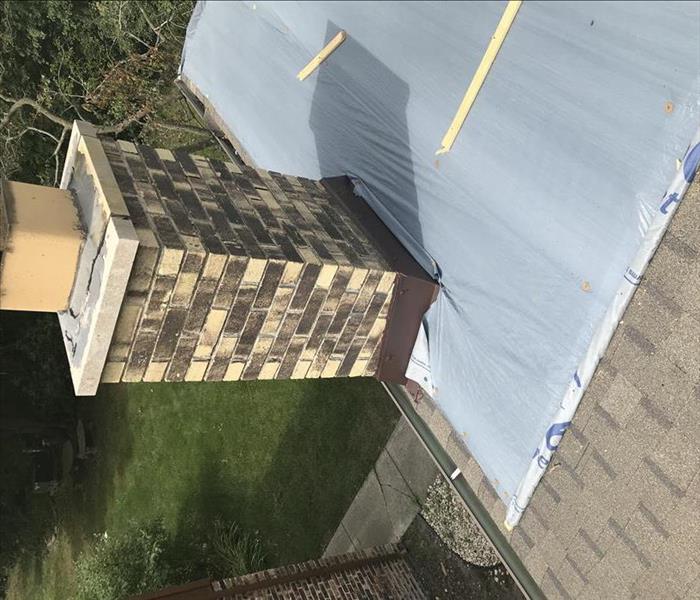 man putting a tarp on a roof around a chimney after a storm