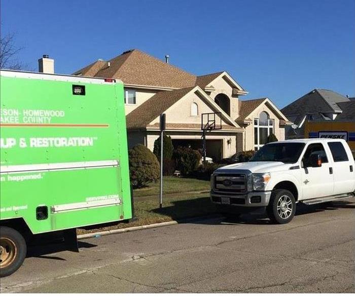 Green SERVPRO truck and a white truck outside of a brown home 